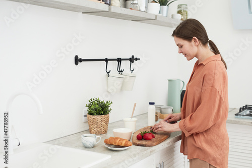 Young woman cutting fruits on the board standing in the kitchen, she preparing breakfast for herself