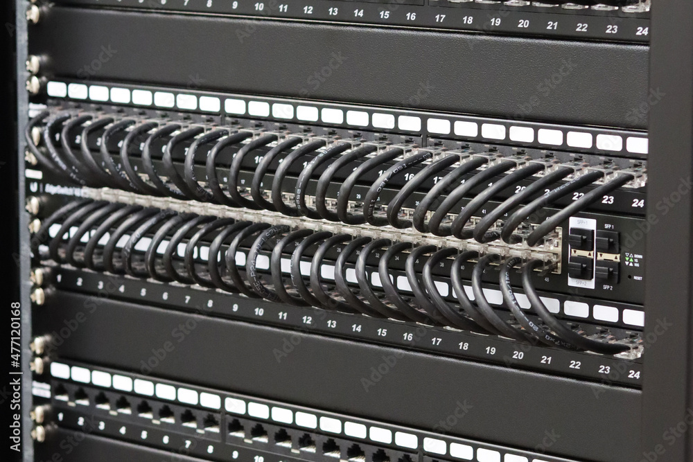 Ethernet switches are connected by black patch cords to patch panels in the data center.