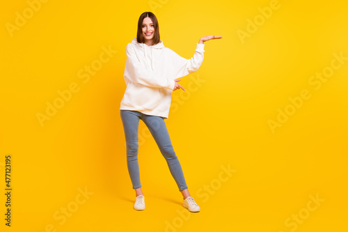 Full length body size view of pretty cheerful girl holding copy space ad demonstrating select isolated over bright yellow color background