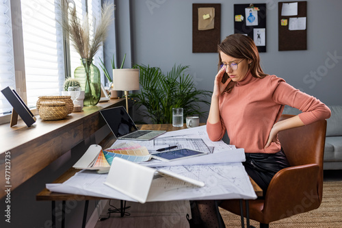 Businesswoman with pain in back. Tired modern woman in the modern house in sunny day having back pain. Shot of a businesswoman suffering from back pain while sitting at her desk