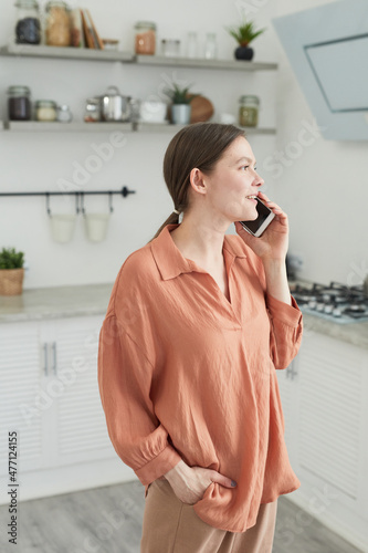 Young woman having a business conversation on mobile phone while standing in the kitchen