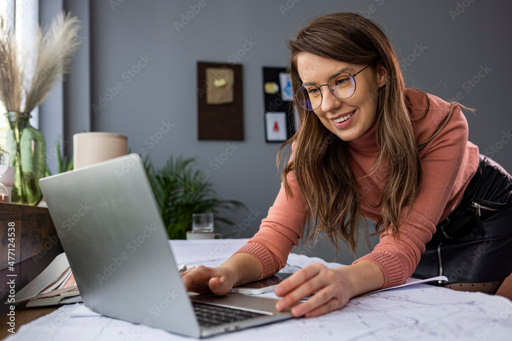Fototapeta premium Confident businesswoman working on laptop at her workplace at modern office.Blurred background. Business woman busy working on laptop computer at office. Cheerful young businesswoman working on laptop