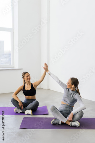 Smiling young fitness women raise hands to give a high five during workout.