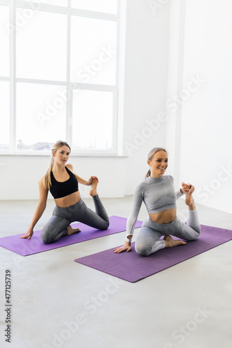 Two attractive sport girls workout yoga pose on mat. Group of young women stretching in gym.