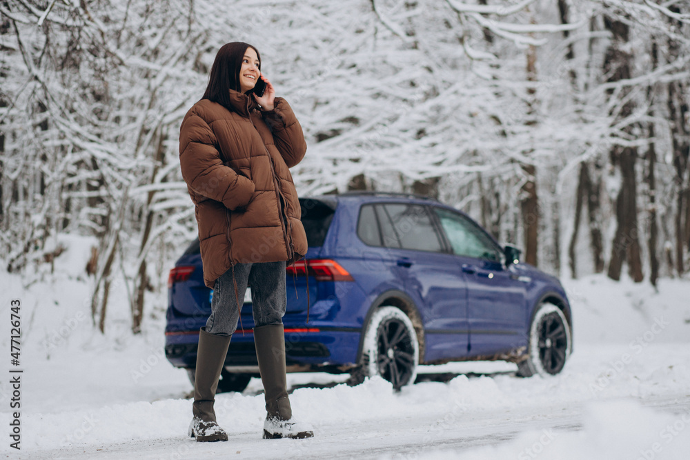 Woman with phone standing by her car in winter forest