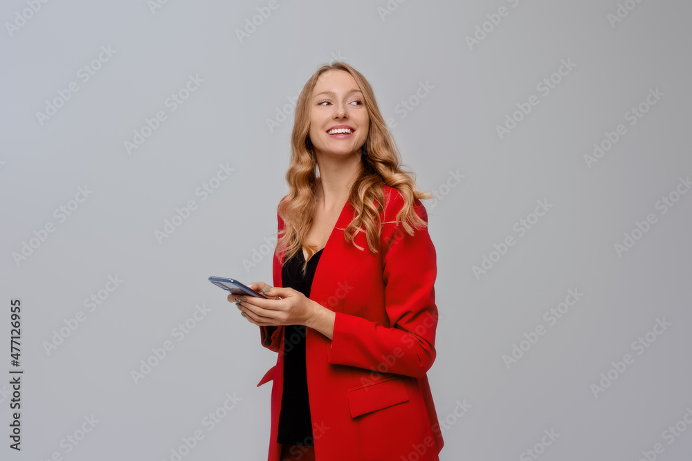 Portrait of successful young woman entrepreneur, holding cellphone her hands, smiling and looking at product with pleased face, standing over gray background Portrait of successful young woman entrepreneur, holding cellphone her hands, smiling and looking at product with pleased face, standing over gray background