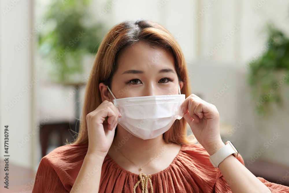 Serious young woman putting on medical mask for protection against coronavirus and pollution Serious young woman putting on medical mask for protection against coronavirus and pollution