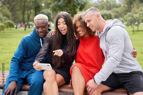 Multi ethnic friends outdoor taking a selfie on smartphone. Diverse group people Afro american asian spending time together Multiracial male female student sitting bench park outdoors © Andrii