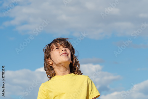 handsome young guy with long hair looks up on a sunny day. blue sky background with clouds