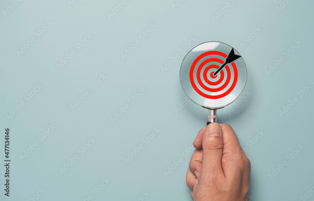 Hand holding magnify glass with red target board inside for focus and setup business objective target concept. - obrazy, fototapety, plakaty 