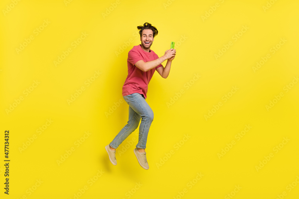 Full body profile photo of cool beard young guy run hold telephone wear red t-shirt jeans footwear isolated on yellow background