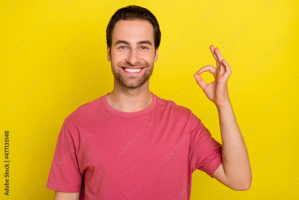 Photo of cheerful glad guy show okey symbol beaming smile wear pink t-shirt isolated yellow color background Photo of cheerful glad guy show okey symbol beaming smile wear pink t-shirt isolated yellow color background