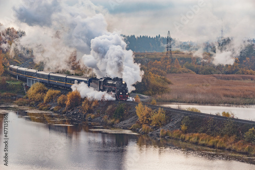 Retro steam train moves along the lake at autumn cloudy morning. Republic of Karelia.