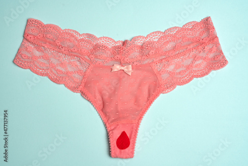 Pink female underwear with a red fake blood drop, isolated on blue.