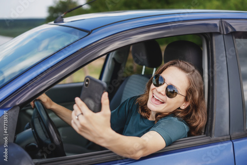 Beautiful young woman in sunglasses smiling communicating video call using smartphone while sitting in car
