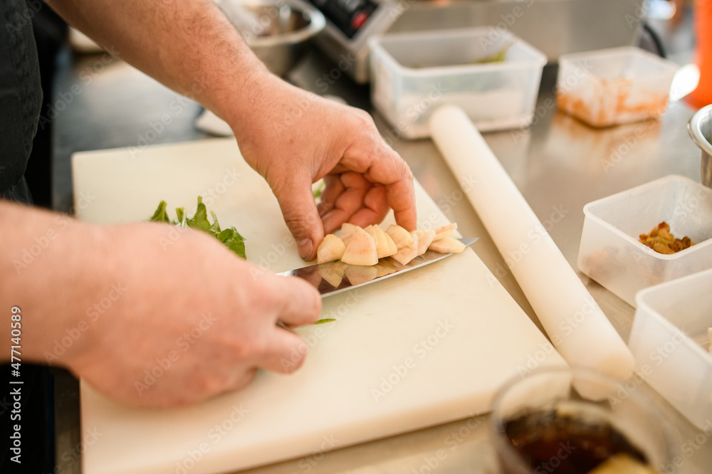 close-up on the hands of a man chef who neatly puts a vegetable on a knife