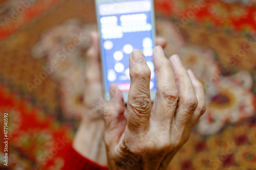 Fototapeta Naklejka Na Ścianę i Meble -  POV of fingers of old woman playing on smartphone in evening in village house (focus on the forefinger in foreground)