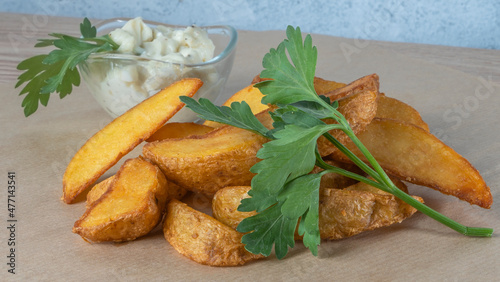 Top view of potato wedges with sauce and parsley on parchment.