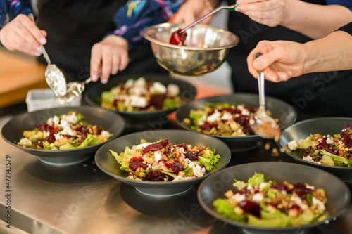 view on plates with salad and hands of people which adds ingredients. Buffet and catering concept