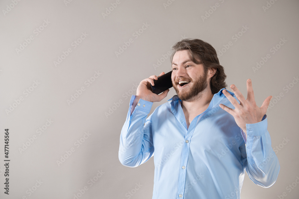 Young bearded man having call and talking on smartphone with pleasure isolated over grey background