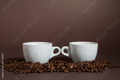 two cups of coffee on a pile of coffee beans on a brown background.
