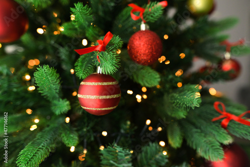 Red Christmas ball on a Christmas tree with garland. Close-up of decorated Christmas tree. Red and golden balls and garland lit with flashlights.