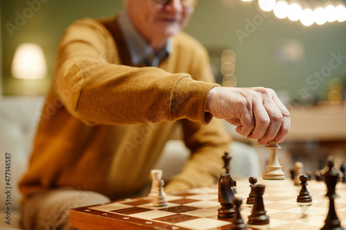 Unrecognizable Caucasian aged man sitting in front of wooden chess board with chess piece in his hand