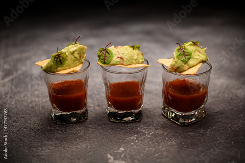 Nachos with guacamole sauce on glass with tomato shots