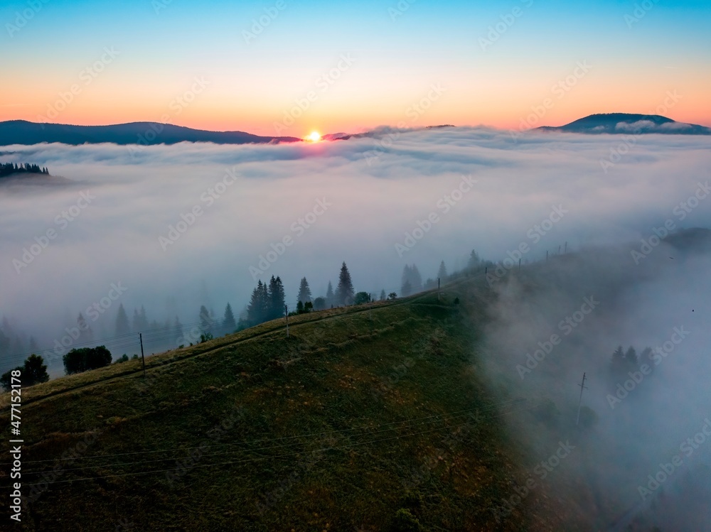 Obraz premium Fog spreads over the mountains at dawn. The sun rises on the horizon. Ukrainian Carpathians in the morning. Aerial drone view.
