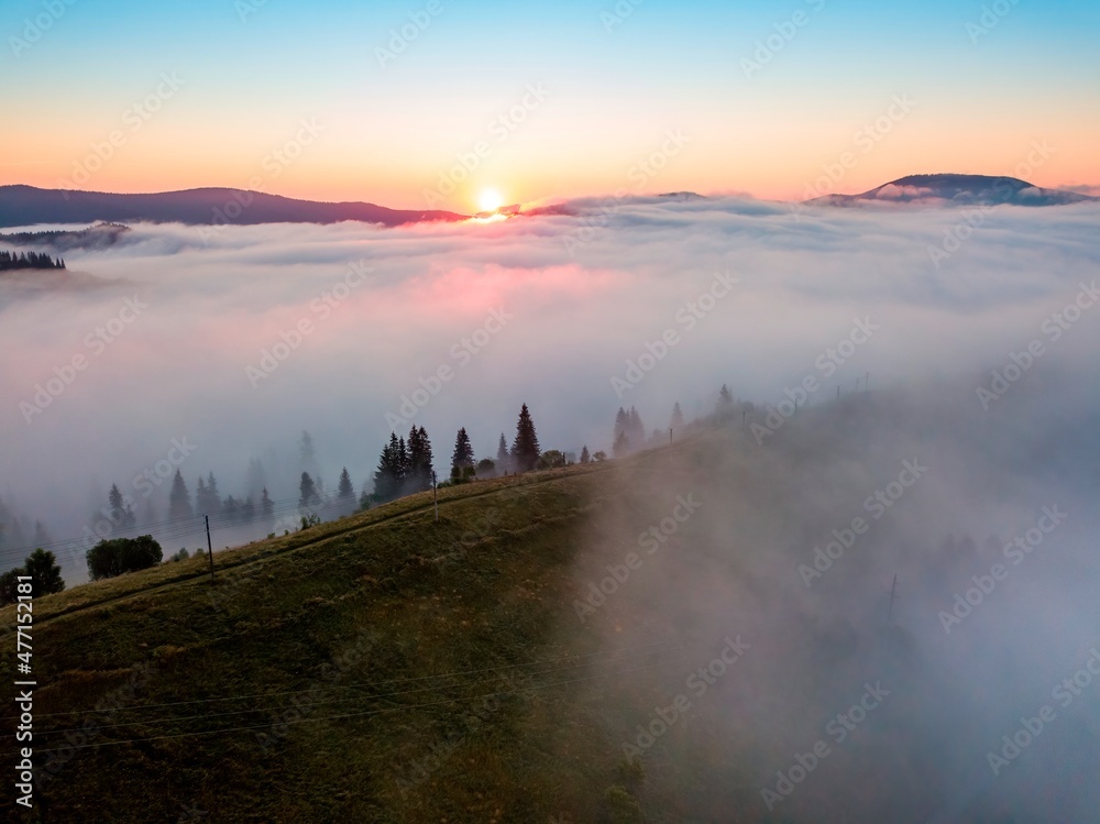 Fog spreads over the mountains at dawn. The sun rises on the horizon. Ukrainian Carpathians in the morning. Aerial drone view.