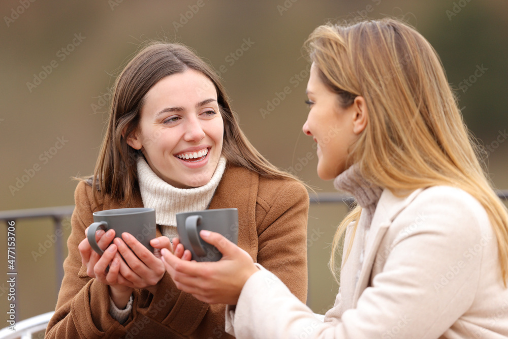 Two happy friends drinking and talking in winter Two happy friends drinking and talking in winter