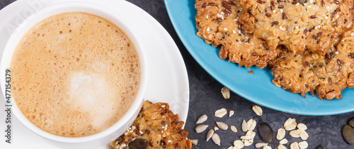 Cup of coffee with milk and fresh baked oatmeal cookies on blue plate. Delicious crunchy dessert