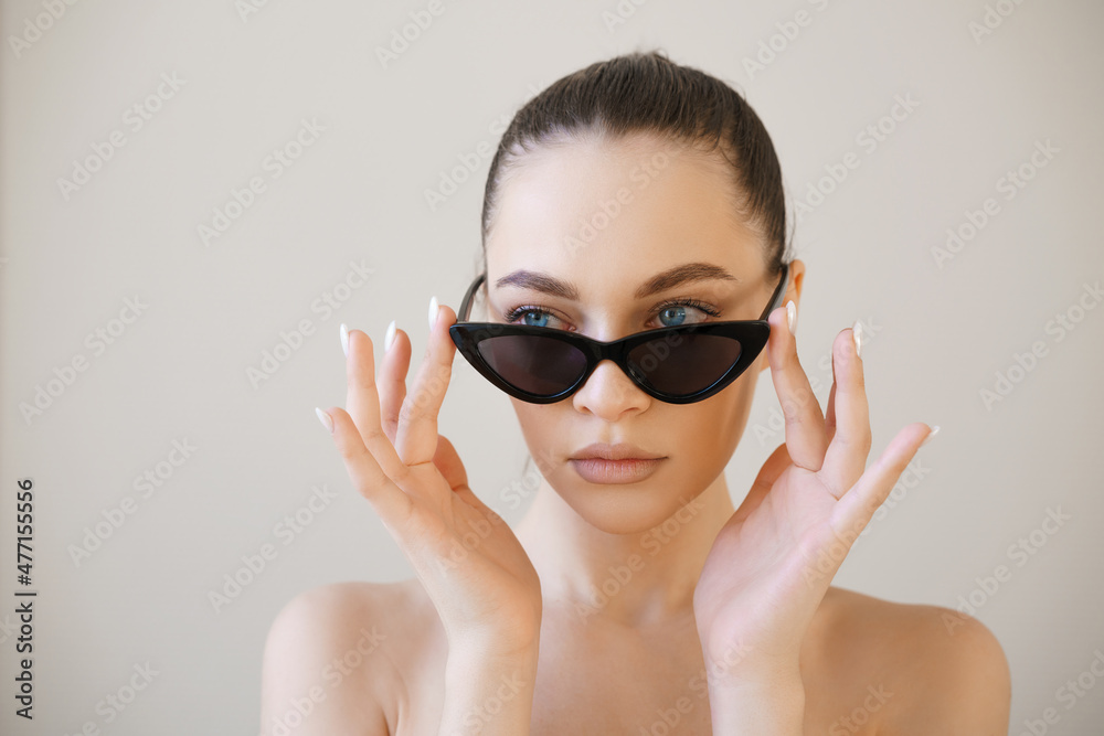 Woman face in sunglasses. Girl face close up portrait of woman. Young girl on light background touches his glasses with his hands. Concept - sale of sunglasses. Wearing sun protection glasses. Woman face in sunglasses. Girl face close up portrait of woman. Young girl on light background touches his glasses with his hands. Concept - sale of sunglasses. Wearing sun protection glasses.