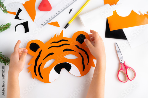 the process of making a children's New Year tiger mask with a child made of colored paper, top view, symbol 2022, step-by-step photo