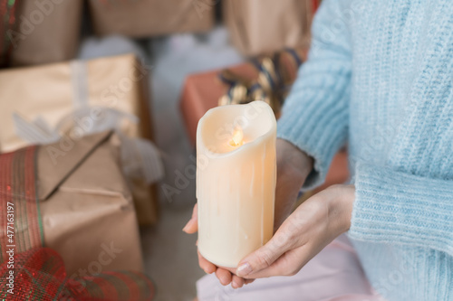 Woman in light blue sweater holding thick white wax candle in her hands. Christmas holiday. Female hands with wax candle. Copy space, close up