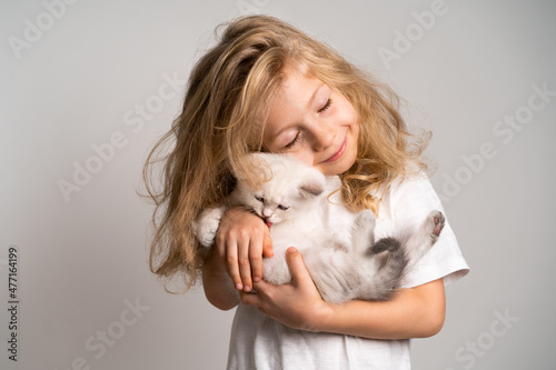 a little blonde girl hugs a cute white kitten who licks her hand, a child and a kitten, a beautiful girl smiles