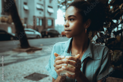 Foto Beautiful young black woman wearing denim shirt in an outdoor restaurant drinking water