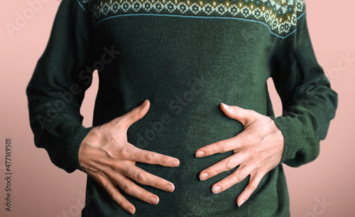 Men holding his big tummy isolated on red background after Christmas dinner Wear green sweater with Holidays overeating concept. photo