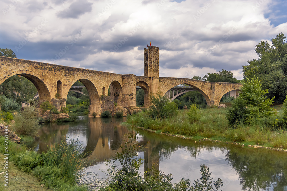 Besalu, Spain, medieval stone bridge with ancient gate, dramatic sky with clouds, mrsta reflection in the water