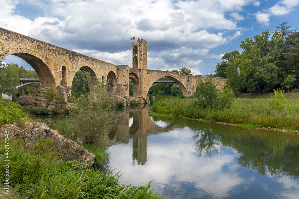 Besalu, Spain, medieval stone bridge with ancient gate, dramatic sky with clouds, mrsta reflection in the water