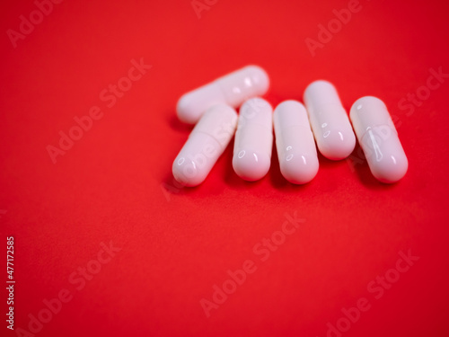 White drug capsules on colored red paper texture background. Macro close up pill medication. Big pharma. Off label approved medicine drugs use. Pharmacy concept. Copy space. Mock up design template.
