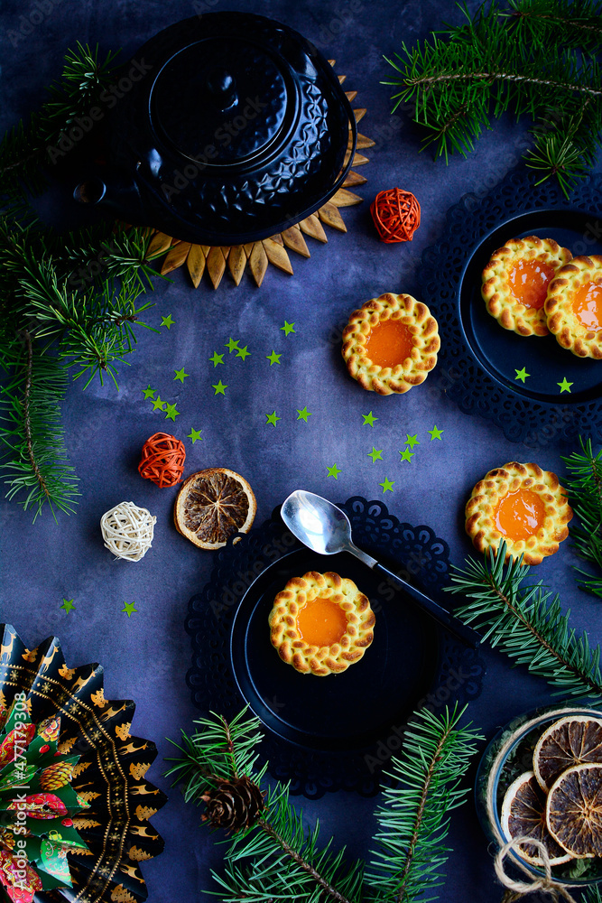 Vertical New Year's layout. Cookies with orange jam filling, teapot, fir branches and decor on a dark gray background. Top view Vertical New Year's layout. Cookies with orange jam filling, teapot, fir branches and decor on a dark gray background. Top view