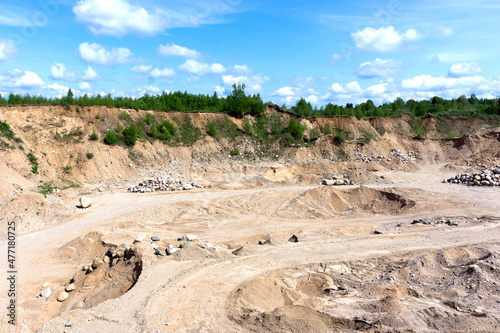 General view of the sand pit. A sunny day. Trees grow along the edge of the quarry. traces of vehicles are visible at the bottom of the quarry.