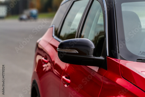Close up front view of car side mirror. Front rear view mirror on the car window. Car exterior details. Red car mirror. © Roman