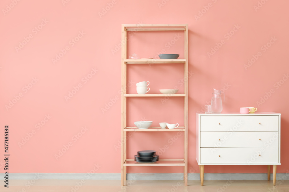 Fototapeta premium Shelving unit and chest of drawers with dishes near pink wall