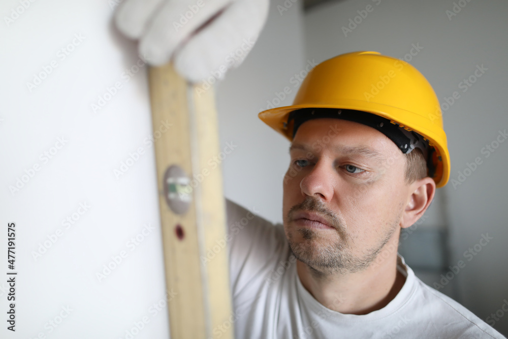 Man in helmet measuring wall using building level in apartment Man in helmet measuring wall using building level in apartment