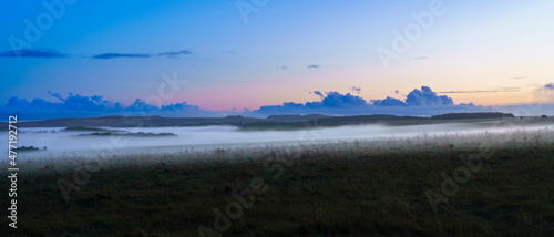 a blanket of ground fog rolling across meadows and woodland in the valley with a red, pink, orange and blue sunset sky, Wiltshire UK