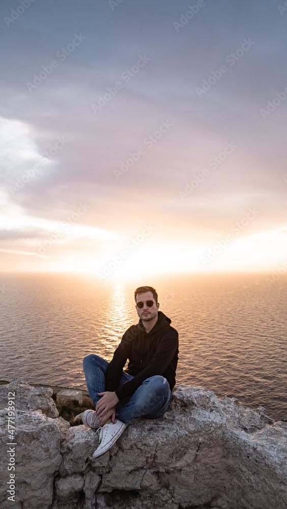 person sitting on the clif during sunset dingli window