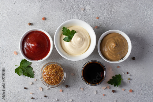 Set of sauces - ketchup, mayonnaise, mustard, soy sauce and mustard seeds on light gray background. View from above