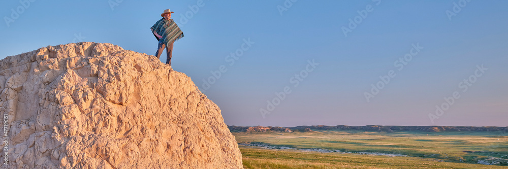 Man in a Mexican poncho and cowboy hat is enjoying summer sunrise at prairie - Pawnee National Grassland in Colorado, panoramic web banner
